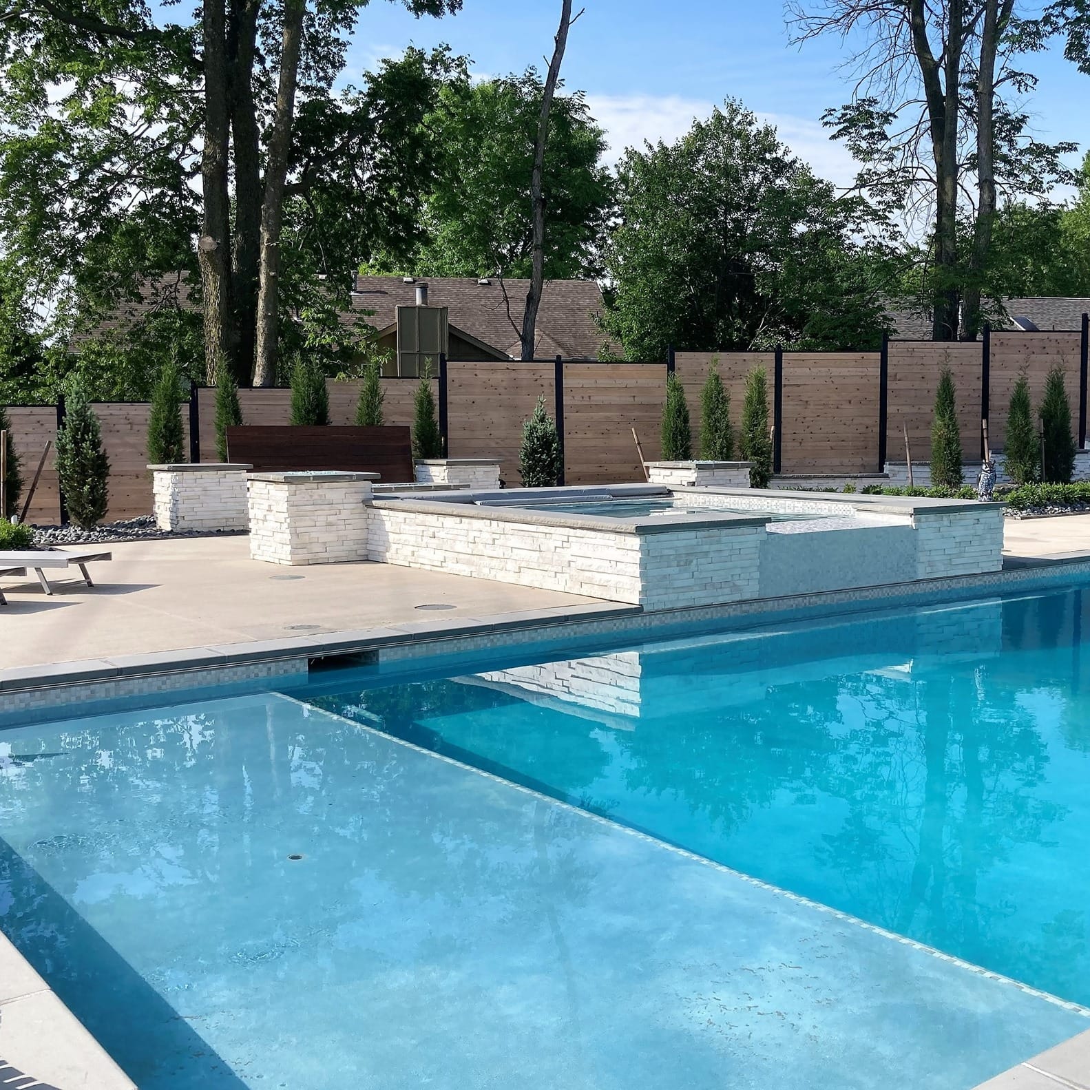 A modern rectangular pool with a raised spa in a fenced backyard